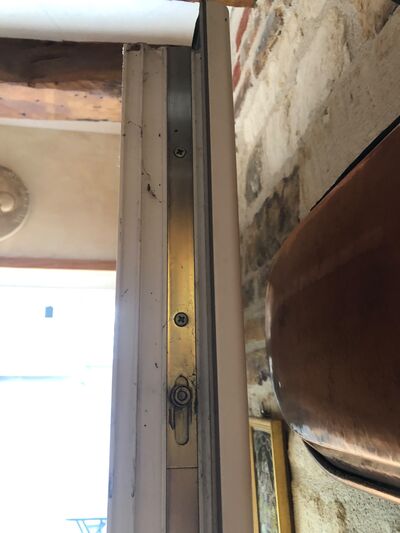 Gâche filante en laiton fixée sur un dormant, mur de brique apparent