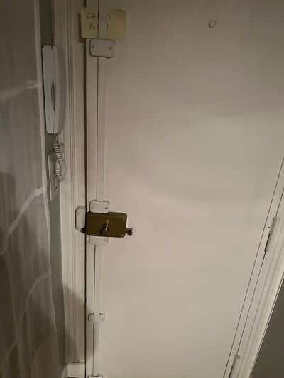 Verrou en applique sur une porte palière blanche, paumelles visibles